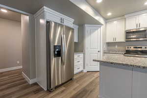 Kitchen with dark hardwood / wood-style flooring, light stone counters, a textured ceiling, stainless steel appliances, and white cabinetry