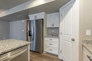 Kitchen featuring white cabinets, light hardwood / wood-style floors, light stone countertops, and stainless steel appliances