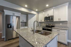 Kitchen with white cabinetry, a kitchen island with sink, dark hardwood / wood-style floors, and appliances with stainless steel finishes