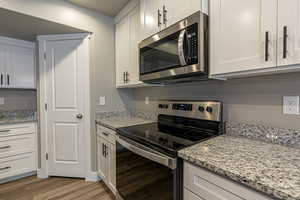 Kitchen featuring white cabinets, appliances with stainless steel finishes, light wood-type flooring, and light stone countertops