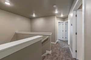 Hall featuring a textured ceiling and dark colored carpet