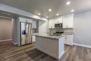 Kitchen with light stone counters, white cabinetry, a kitchen island with sink, and appliances with stainless steel finishes