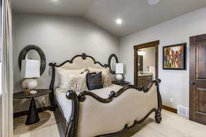 Bedroom featuring light colored carpet, ensuite bath, and lofted ceiling