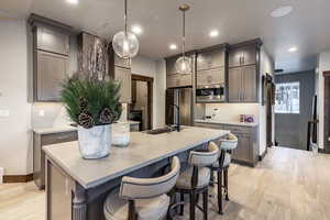 Kitchen with backsplash, a kitchen island with sink, sink, appliances with stainless steel finishes, and decorative light fixtures