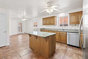 Kitchen featuring dishwasher, sink, ceiling fan, a textured ceiling, and a kitchen island