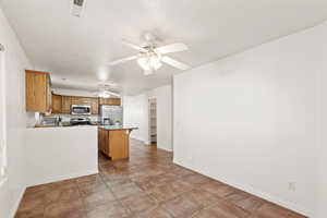 Kitchen with kitchen peninsula, appliances with stainless steel finishes, ceiling fan, light tile patterned floors, and a breakfast bar area