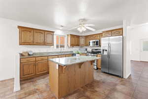 Kitchen featuring a kitchen bar, appliances with stainless steel finishes, ceiling fan, sink, and a kitchen island