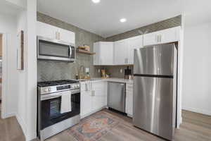 Kitchen with white cabinets, decorative backsplash, light hardwood / wood-style floors, and stainless steel appliances