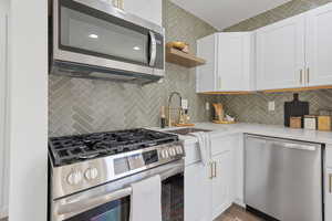 Kitchen with backsplash, white cabinets, and appliances with stainless steel finishes