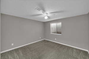 Carpeted empty room with ceiling fan and a textured ceiling