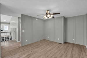 Empty room featuring ceiling fan, light wood-type flooring, a textured ceiling, and lofted ceiling