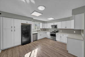 Kitchen with sink, stainless steel appliances, tasteful backsplash, white cabinets, and light wood-type flooring