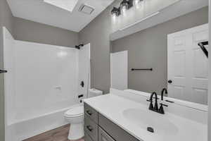 Full bathroom with a skylight, bathtub / shower combination, vanity, hardwood / wood-style flooring, and toilet