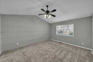 Carpeted empty room featuring vaulted ceiling and ceiling fan