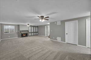 Unfurnished living room featuring a textured ceiling, light colored carpet, and ceiling fan