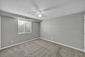 Empty room with ceiling fan, carpet floors, and a textured ceiling