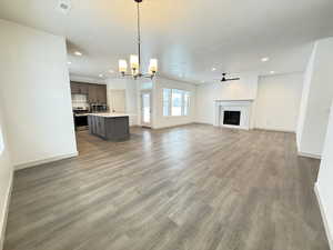 Unfurnished living room featuring ceiling fan with notable chandelier and hardwood / wood-style flooring