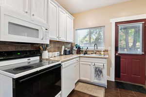 Kitchen with white appliances, white cabinets, dark tile patterned flooring, sink, and tasteful backsplash