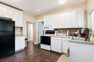 Kitchen with tasteful backsplash, white cabinetry, sink, and white appliances