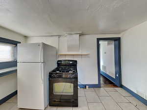 Kitchen featuring black gas range, white refrigerator, a textured ceiling, and light tile patterned flooring