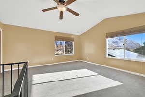 Carpeted spare room with a mountain view, vaulted ceiling, plenty of natural light, and ceiling fan