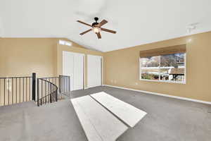 Interior space with ceiling fan, lofted ceiling, and dark colored carpet