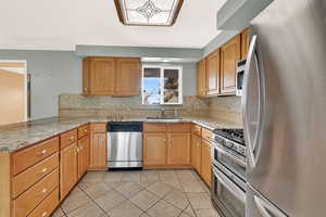 Kitchen with light stone countertops, sink, kitchen peninsula, light tile patterned floors, and appliances with stainless steel finishes