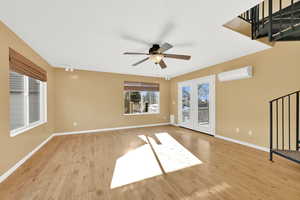 Unfurnished living room featuring light wood-type flooring, a wall mounted AC, and ceiling fan