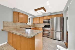 Kitchen with kitchen peninsula, light stone countertops, light tile patterned floors, and appliances with stainless steel finishes