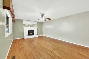 Unfurnished living room featuring a brick fireplace, ceiling fan, and light wood-type flooring