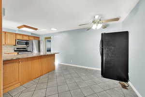 Kitchen featuring decorative backsplash, light stone countertops, light tile patterned floors, kitchen peninsula, and stainless steel appliances