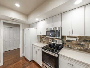 Kitchen featuring tasteful backsplash, white cabinetry, dark hardwood / wood-style floors, and appliances with stainless steel finishes