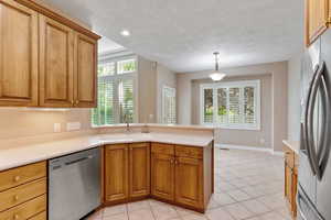 Kitchen with sink, stainless steel appliances, kitchen peninsula, pendant lighting, and light tile patterned flooring