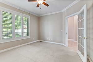 Carpeted empty room featuring ceiling fan, french doors, and ornamental molding