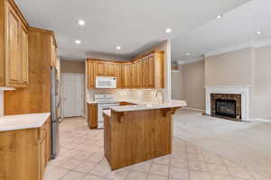 Kitchen featuring kitchen peninsula, light carpet, a high end fireplace, white appliances, and a breakfast bar area