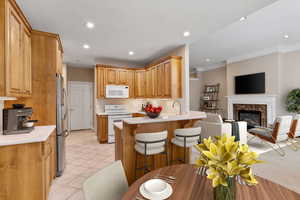 Kitchen with white appliances, a high end fireplace, crown molding, kitchen peninsula, and a breakfast bar area