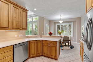 Kitchen with sink, hanging light fixtures, appliances with stainless steel finishes, light tile patterned flooring, and kitchen peninsula