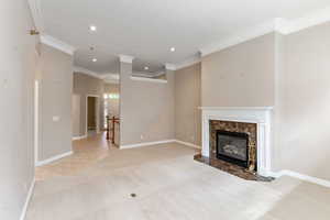 Unfurnished living room featuring a premium fireplace, ornamental molding, and light carpet