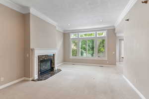 Unfurnished living room featuring a textured ceiling, light colored carpet, ornamental molding, and a fireplace