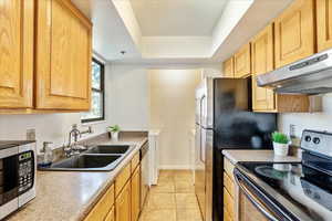 Kitchen with a raised ceiling, sink, light tile patterned floors, appliances with stainless steel finishes, and extractor fan