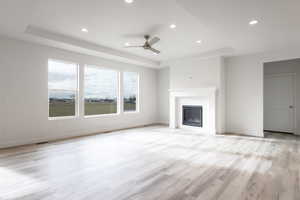 Unfurnished living room featuring ceiling fan, light hardwood / wood-style floors, and a raised ceiling