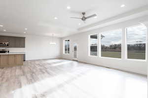 Unfurnished living room with ceiling fan with notable chandelier, a healthy amount of sunlight, light hardwood / wood-style floors, and sink