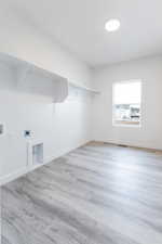 Laundry area with washer hookup, electric dryer hookup, and light hardwood / wood-style floors