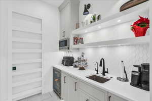 Kitchen featuring decorative backsplash, sink, white cabinetry, wine cooler, and stainless steel microwave