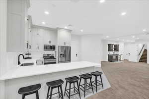 Kitchen featuring kitchen peninsula, a breakfast bar, stainless steel appliances, light colored carpet, and sink