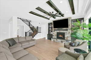 Living room with light wood-type flooring, a raised ceiling, ceiling fan, built in features, and a stone fireplace