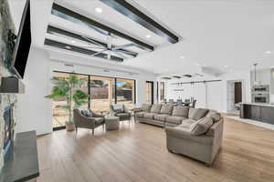 Living room with beamed ceiling, light hardwood / wood-style floors, ceiling fan, and a high end fireplace