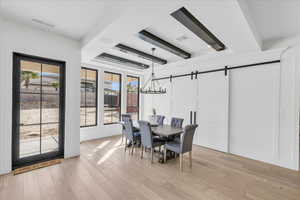 Dining space with a barn door, a chandelier, and light wood-type flooring