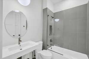 Full bathroom featuring toilet, shower / bath combination with glass door, and sink