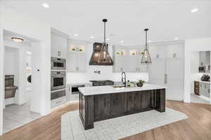 Kitchen with premium range hood, appliances with stainless steel finishes, an island with sink, and light wood-type flooring